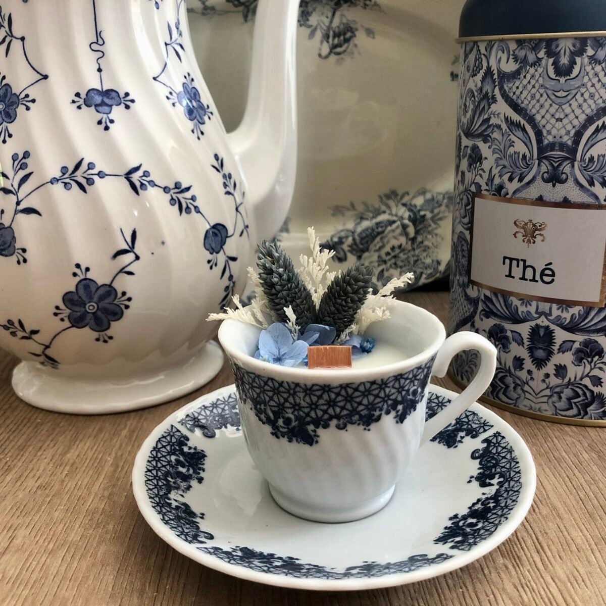 Bougie artisanale dans une tasse de thé et soucoupe vintage avec des fleurs séchées dans les tons bleus et blancs