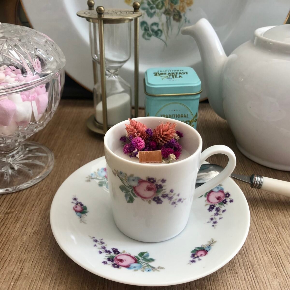 Bougie artisanale dans une petite tasse à café avec sa soucoupe et des fleurs séchées dans les tons roses et violets