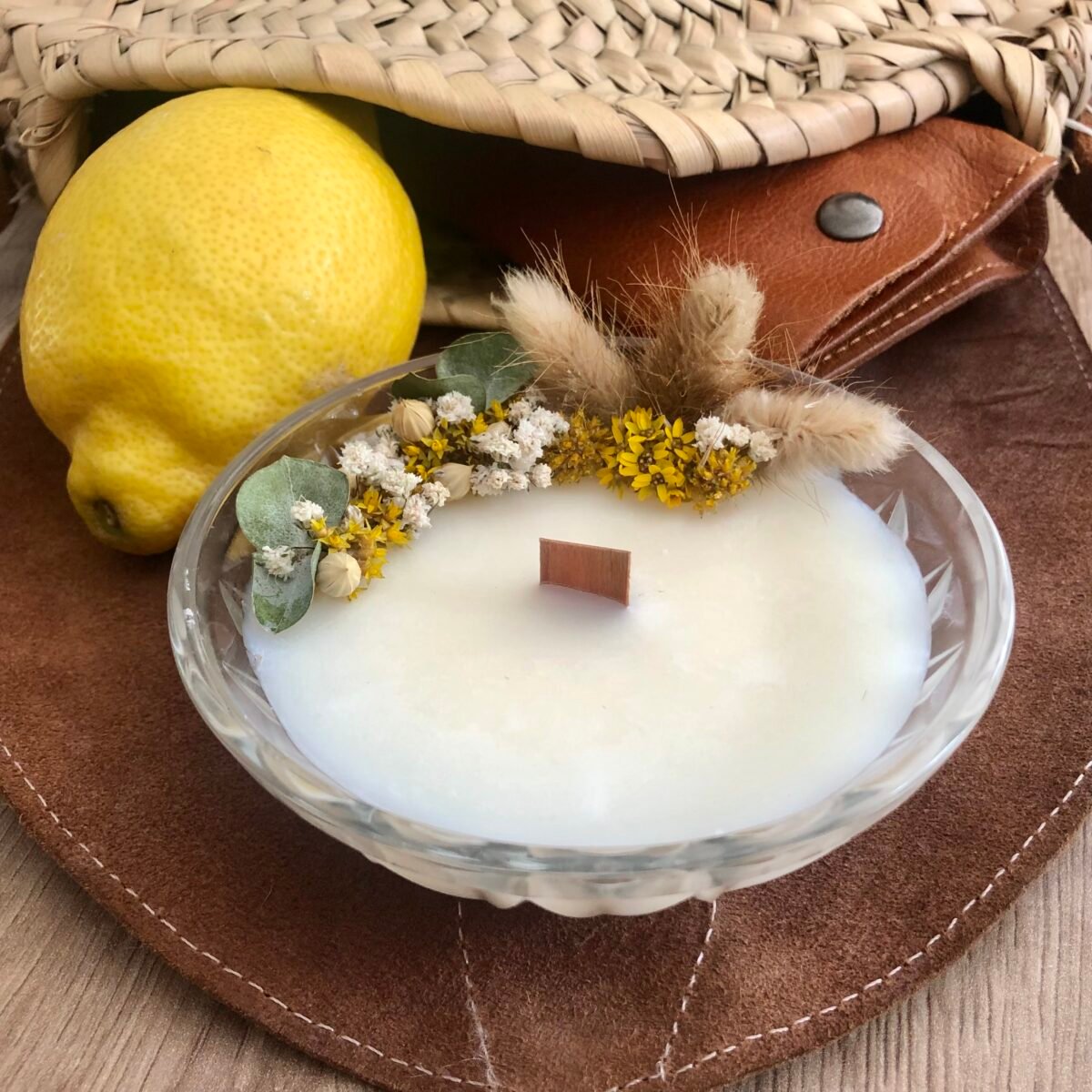 Bougie artisanale avec fleurs séchées jaunes et blanches dans un pot en verre vintage avec un citron et un sac en fond