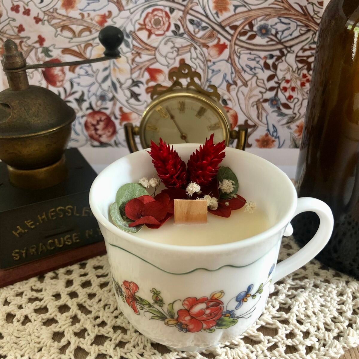 Bougie artisanale dans une tasse à café vintage de nos grands-mères avec des fleurs séchées rouges, blanches et vertes