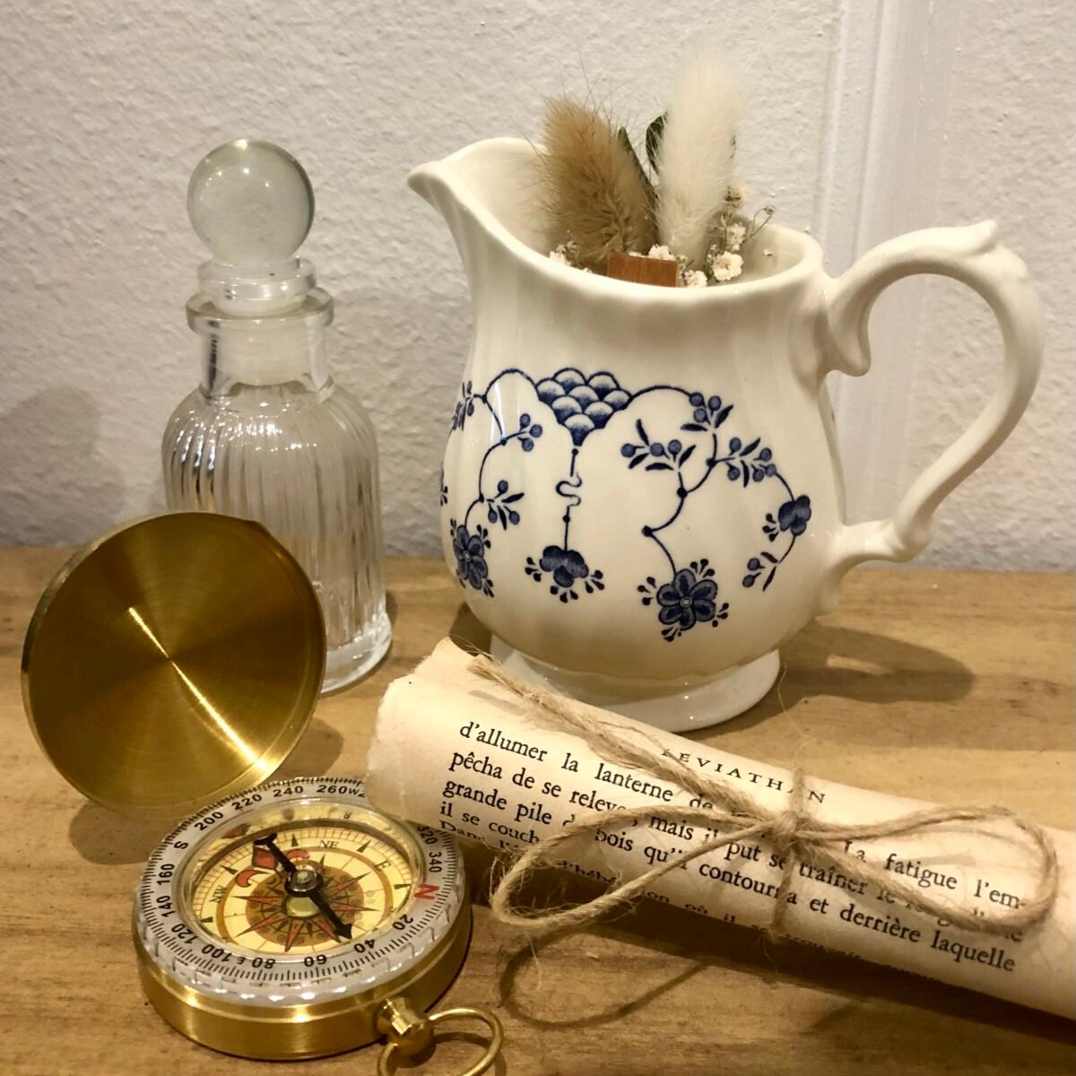 Bougie artisanale dans un petit saucier blanc et bleu avec des fleurs séchées dans les tons blancs