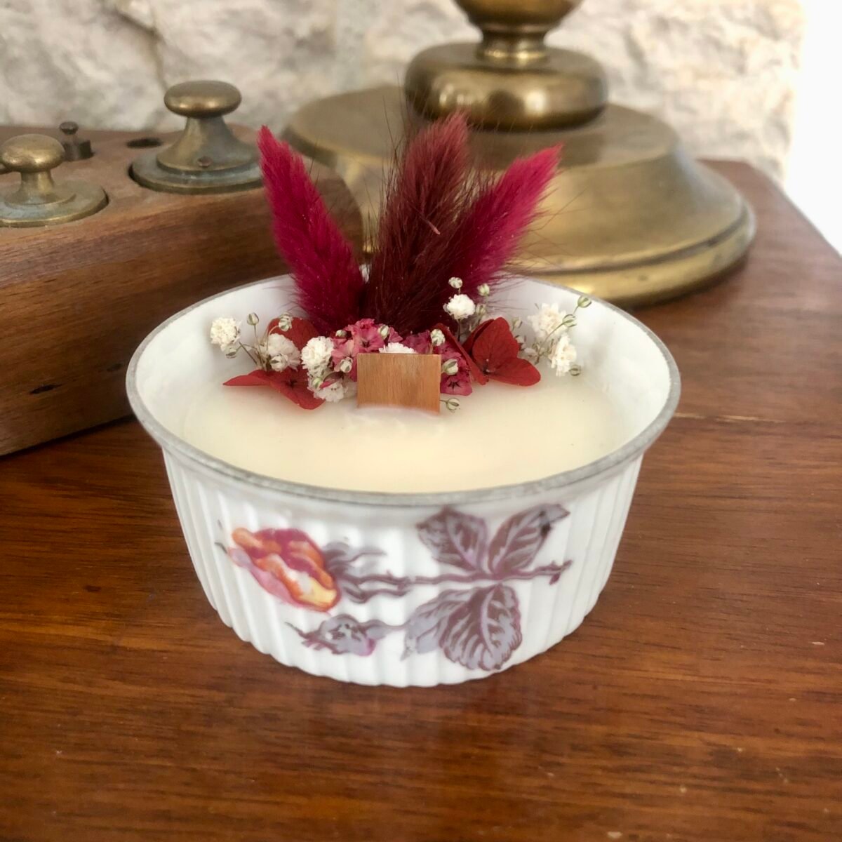 Bougie artisanale dans un petit pot en céramique vintage avec des fleurs séchées dans les tons rouges et roses