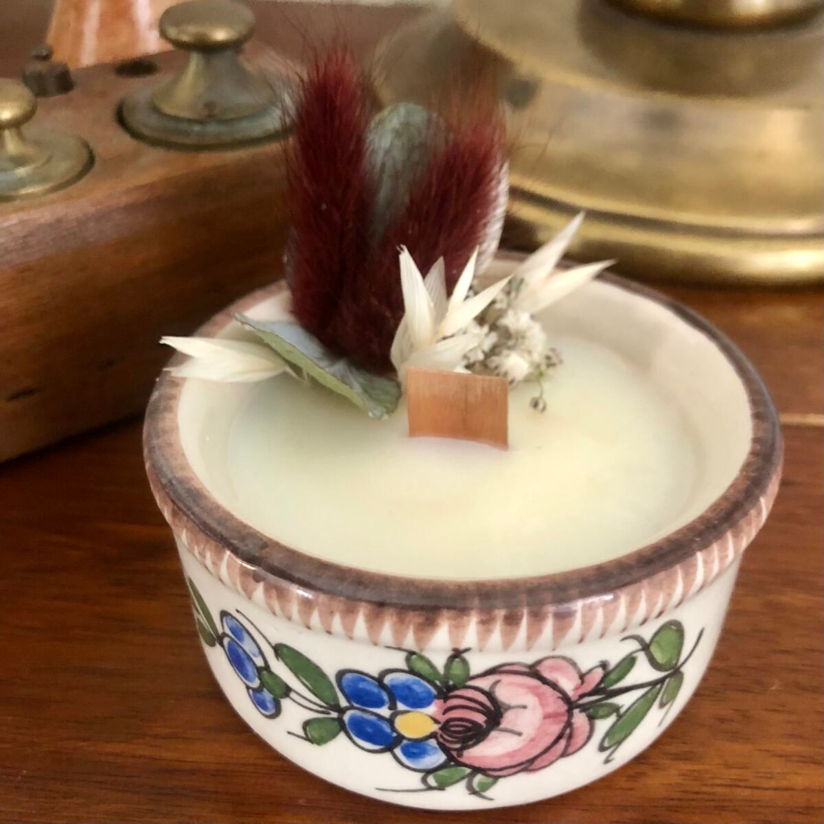 Bougie artisanale dans un petit pot en céramique peint avec des fleurs séchées dans les tons marrons et blancs
