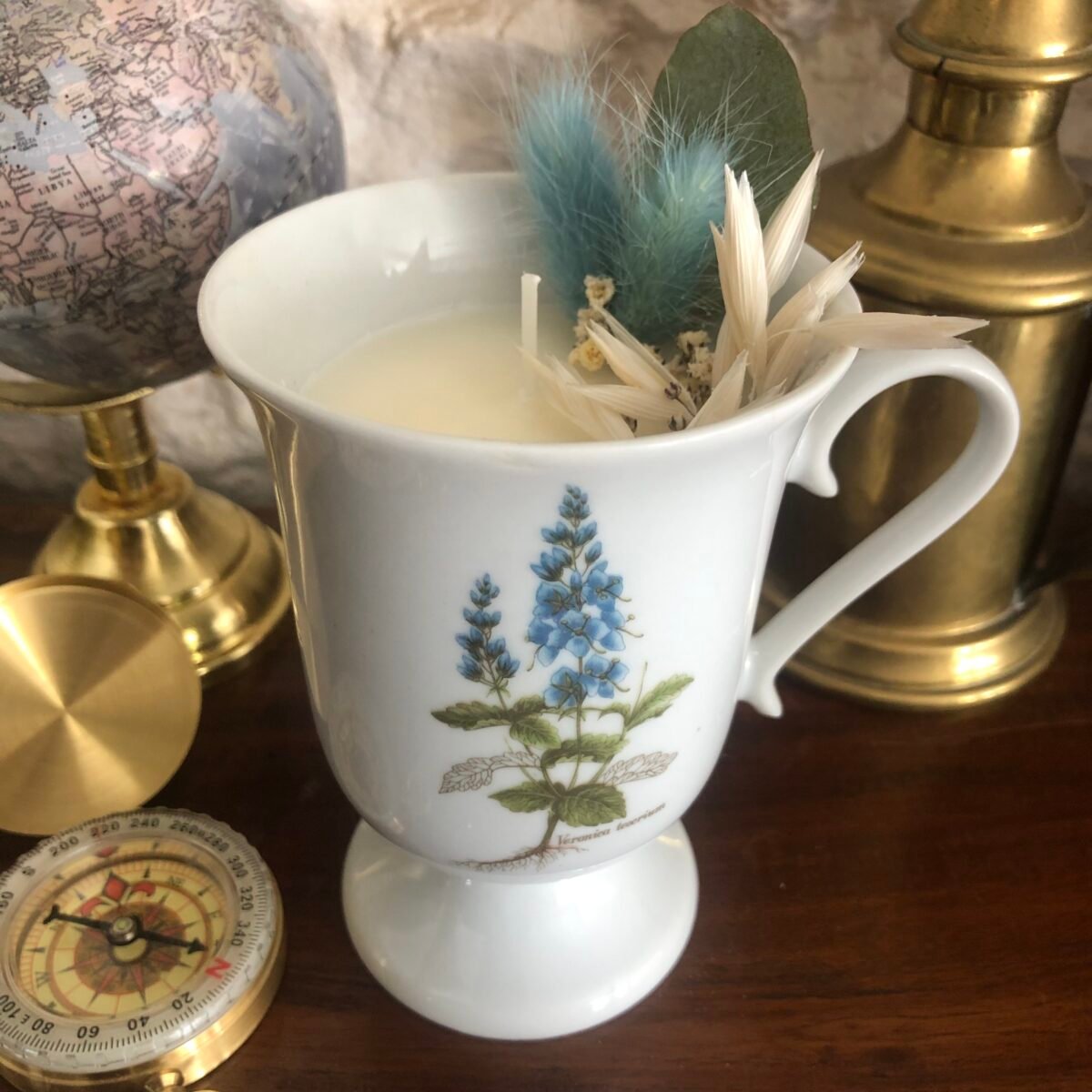 Bougie artisanale dans une tasse à café haute vintage blanche avec des fleurs séchées dans les tons bleus