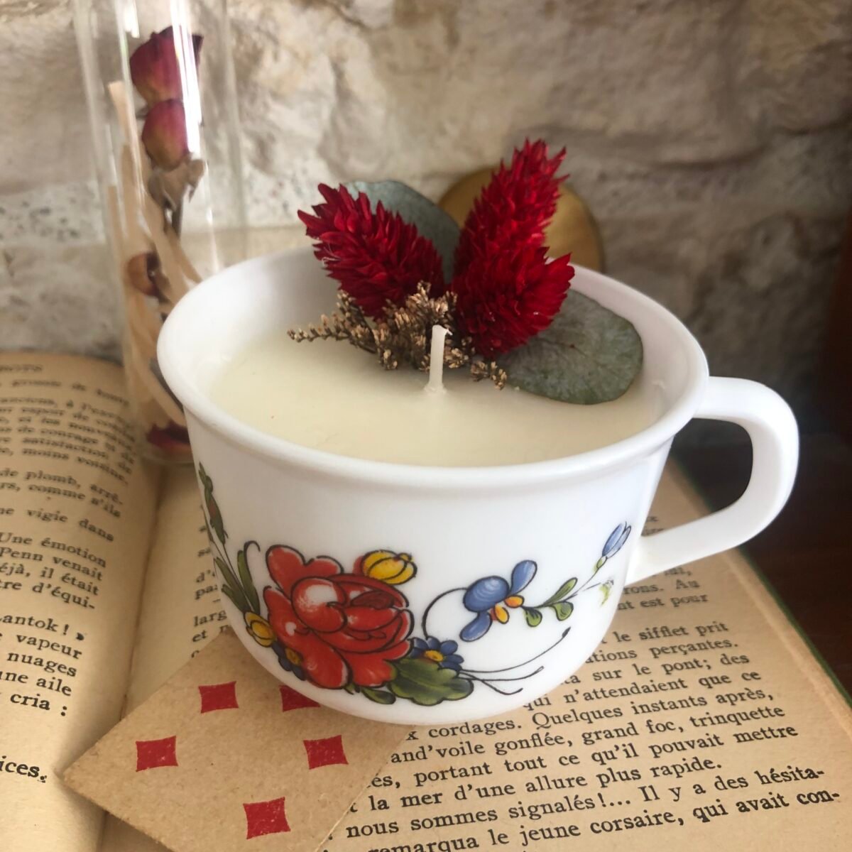 Bougie artisanale dans une tasse à café vintage colorée et fleurs séchées dans les tons rouges