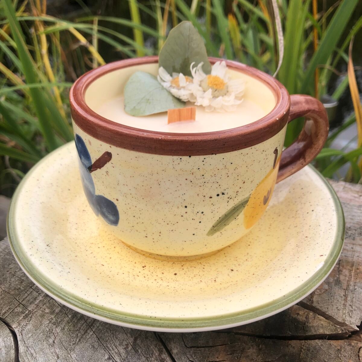 Bougie artisanale dans une très grande tasse à café dans les tons naturels avec des fruits et une soucoupe décorée avec des fleurs séchées sur un fond naturel