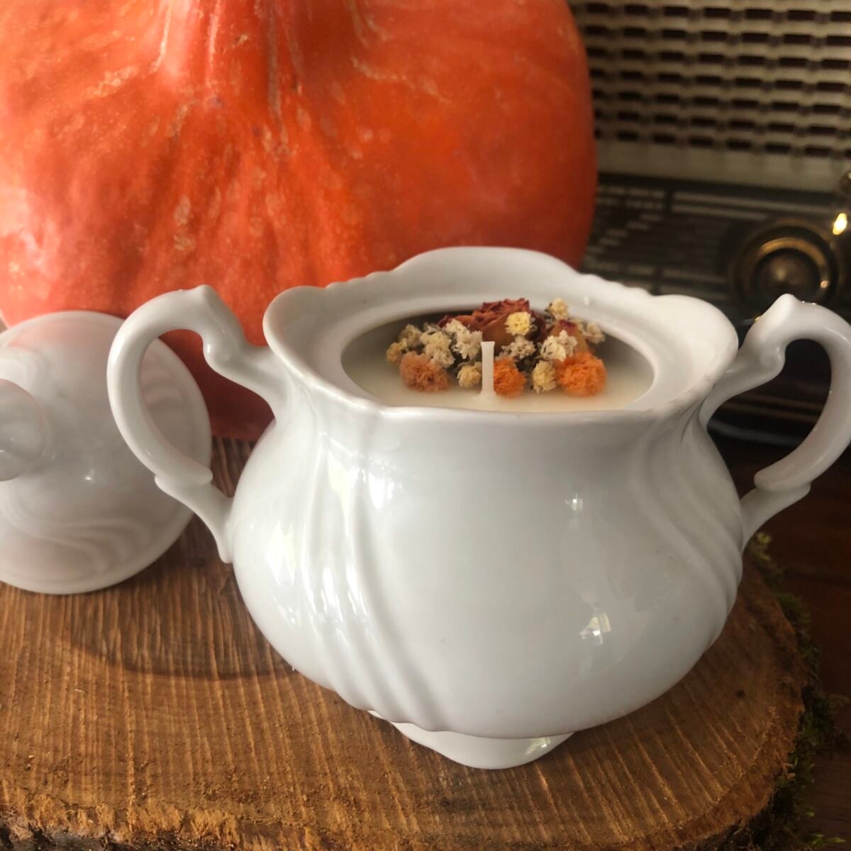 Bougie artisanale dans un pot en céramique blanc vintage et élégant avec son couverte dans des tons automnales oranges